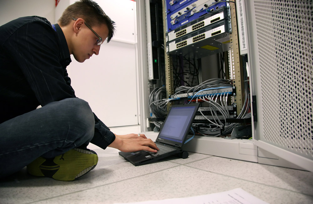 Camera engineer beside network rack with laptop